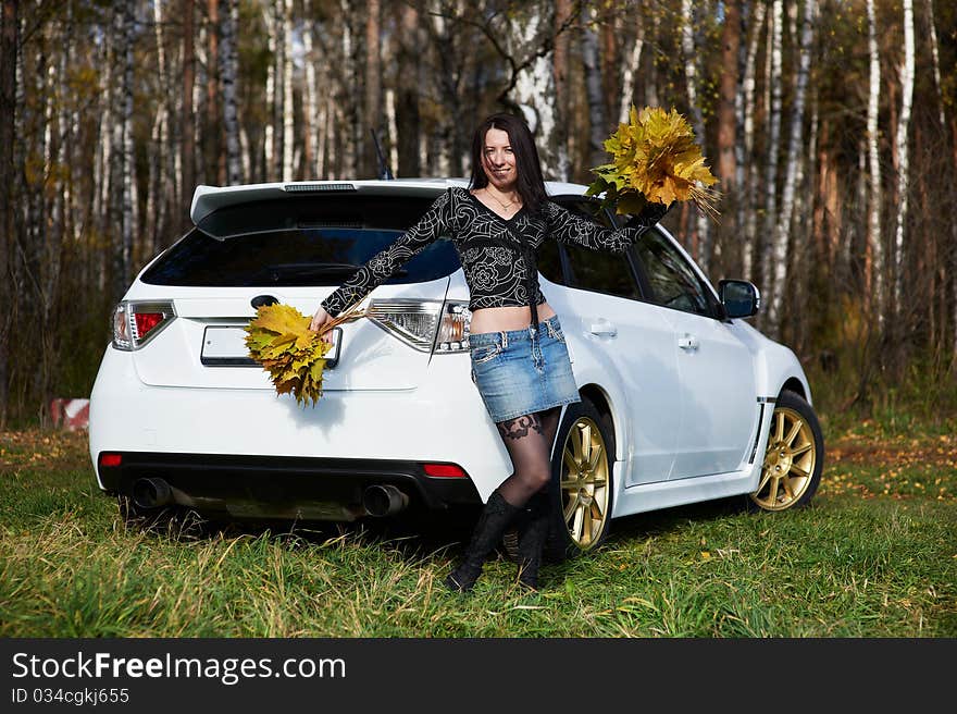 Joyful girl with yellow leaves and white car