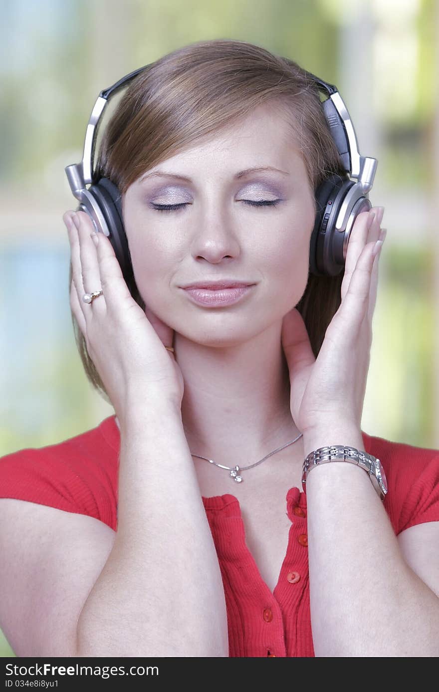 A caucasian woman listens to music on a headset, set against a green window background.