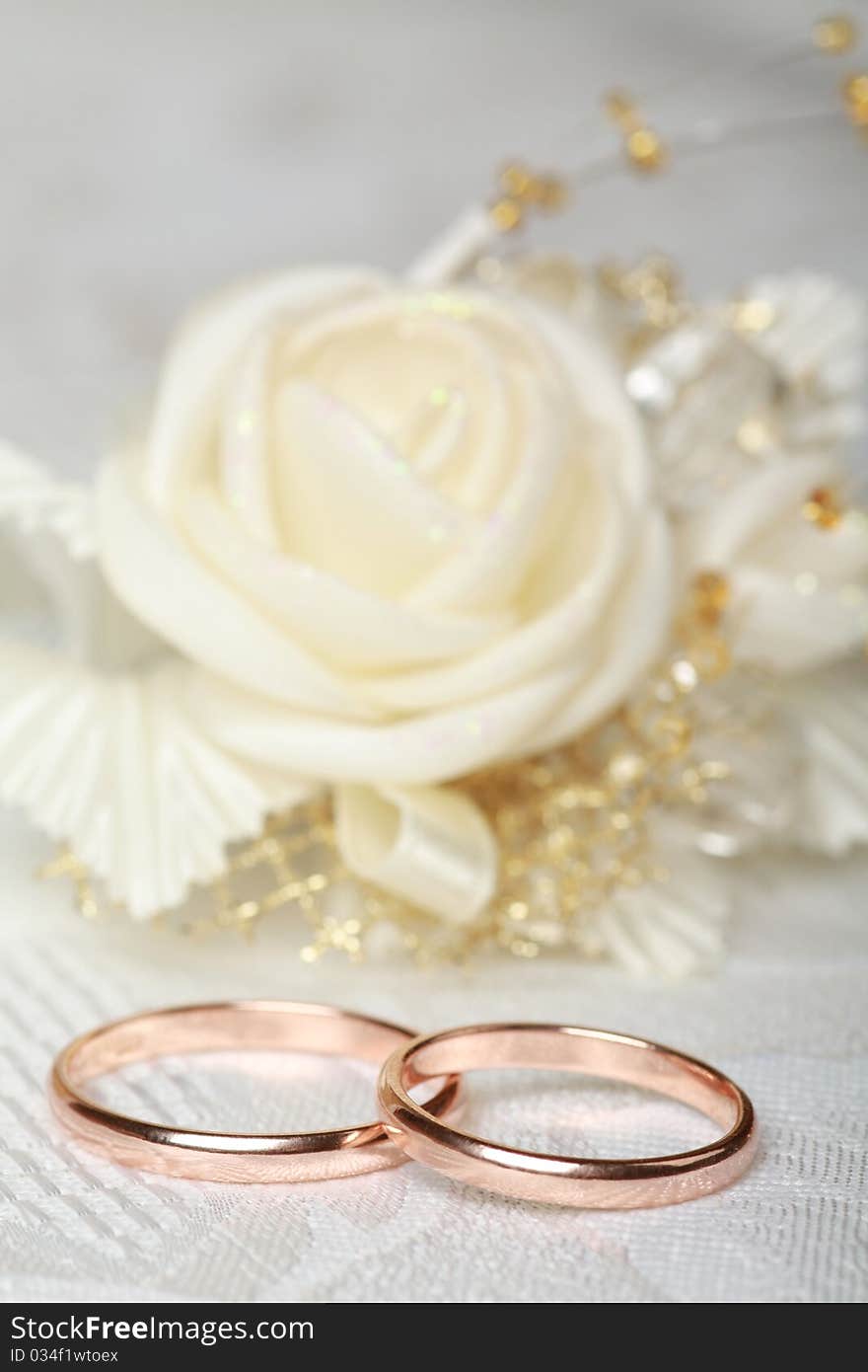 Gold wedding rings and satin rose flower on lace background