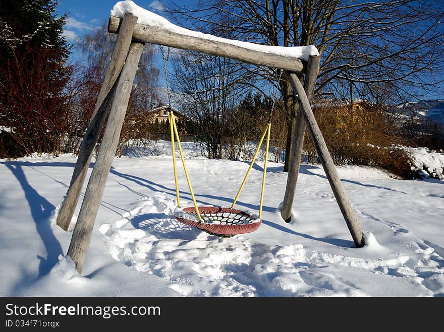 Snow covered swing at empty playground in winter.