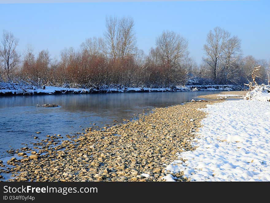 Curved rocky river covered by snow in a sunny winter day