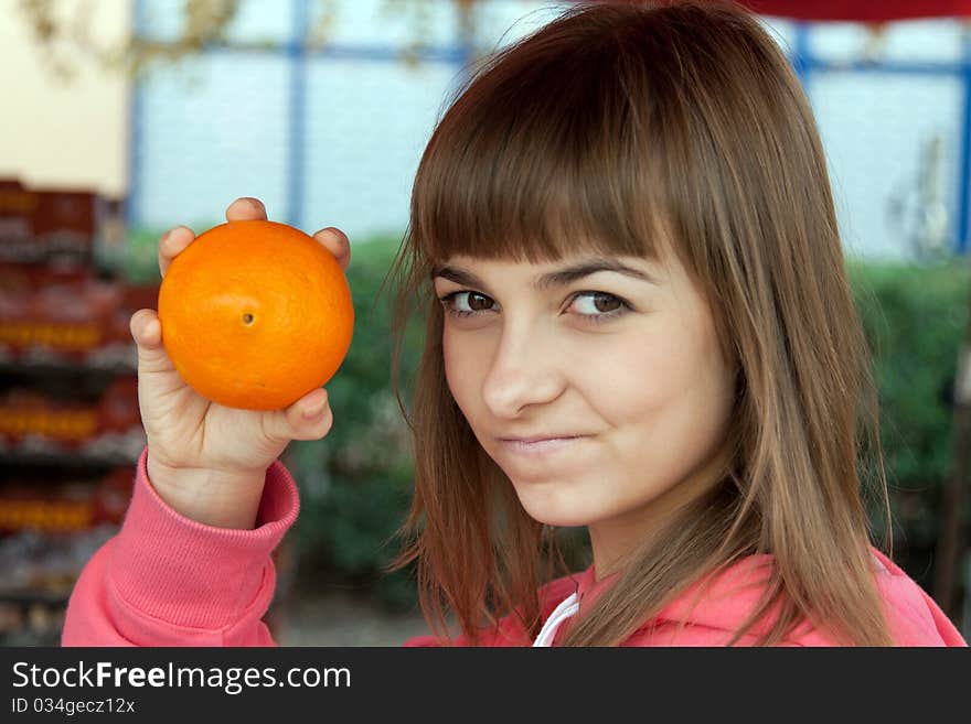 Beautiful girl with an orange at the bazaar