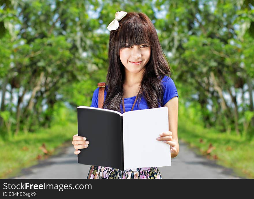 Happy young girl smiling while holding and reading a book. Happy young girl smiling while holding and reading a book