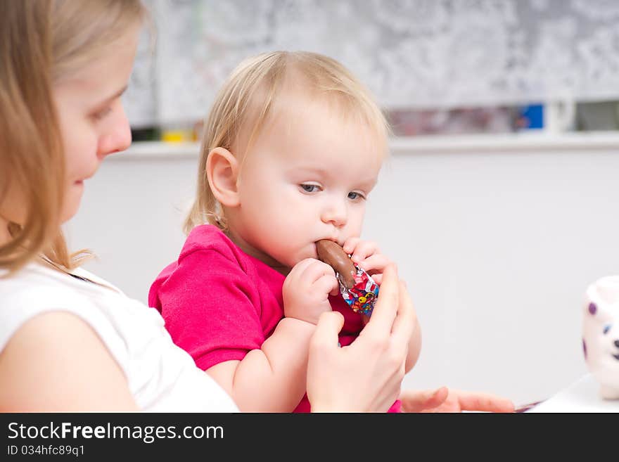 Young adorable baby eat chocolate with mother in kitchen