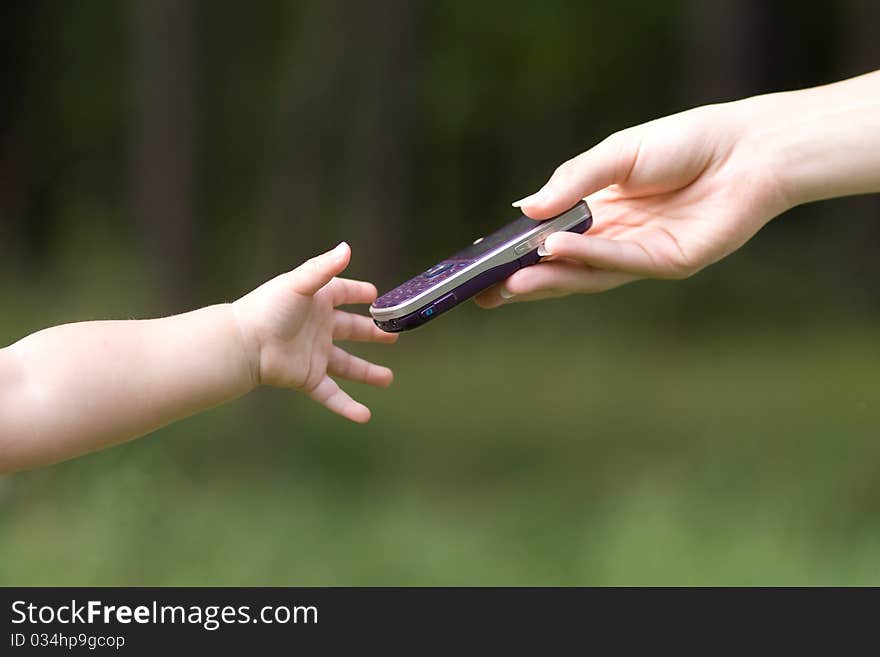 Female hand Giving cellphone to the child`s hand on the forest background