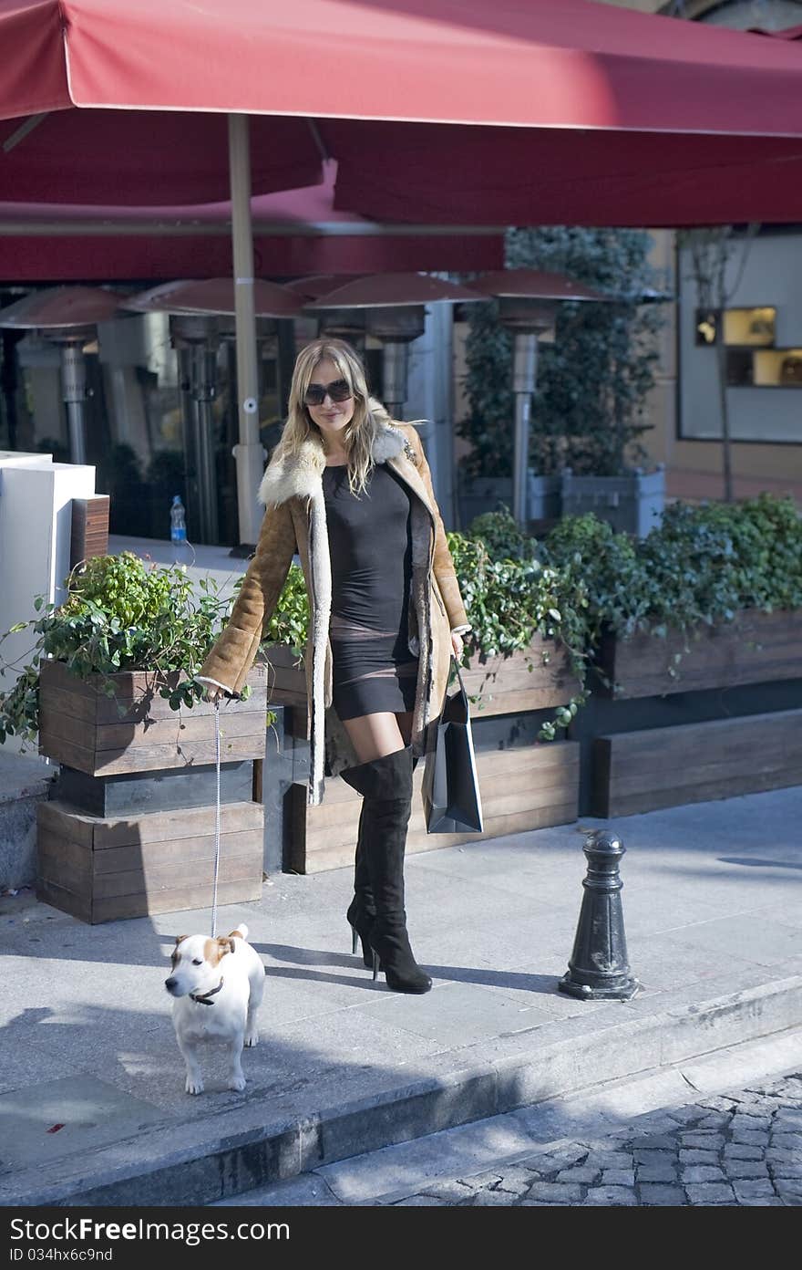 Blond woman walking down the fashion district of a modern city with a jack russel. Blond woman walking down the fashion district of a modern city with a jack russel