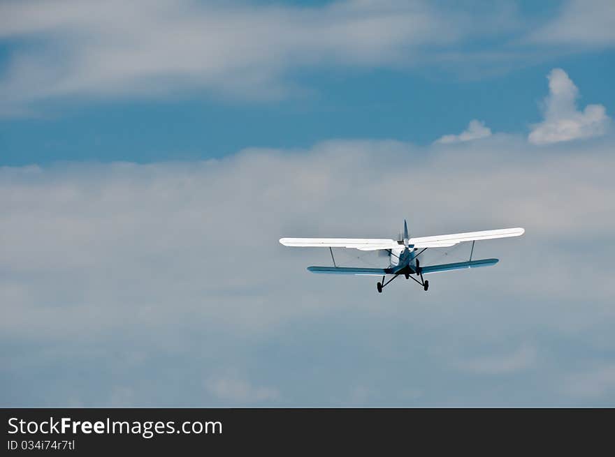 AN-2 airplne flying away in blue, filled with clouds sky. AN-2 airplne flying away in blue, filled with clouds sky