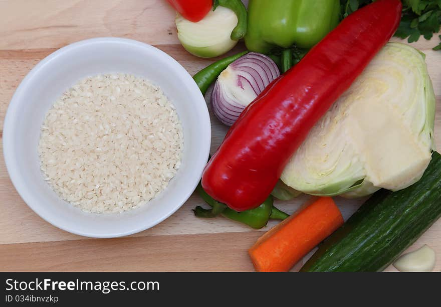 Upper view of a bowl of rice near fresh vegetables on a choping board. Upper view of a bowl of rice near fresh vegetables on a choping board.