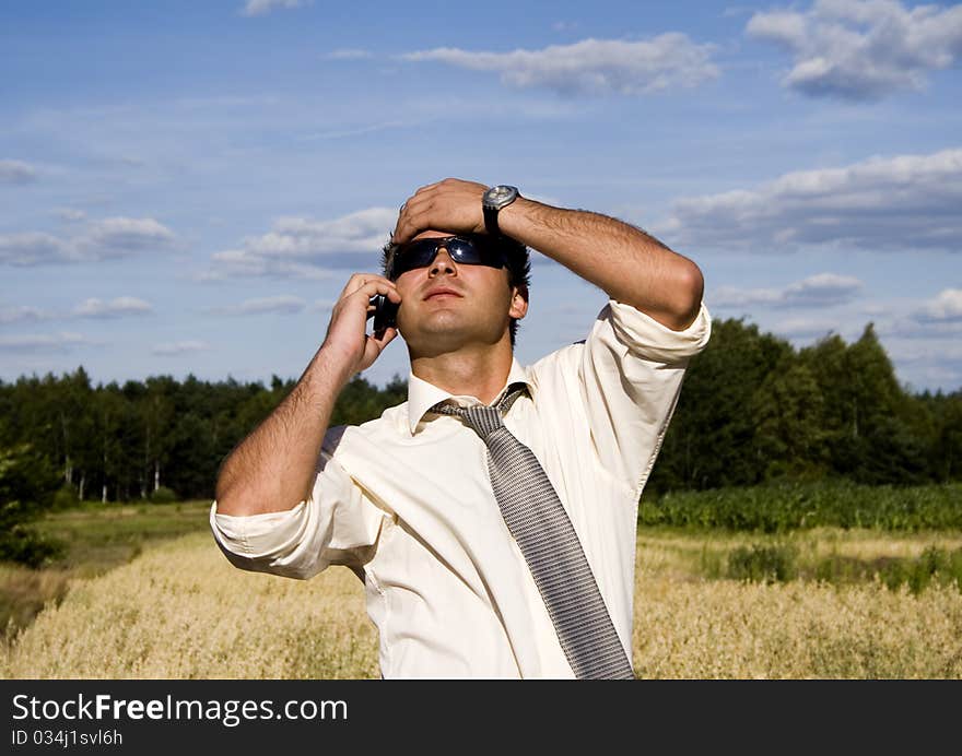 A businessman dressed in a smart suit standing on grass and talking on mobile phone.