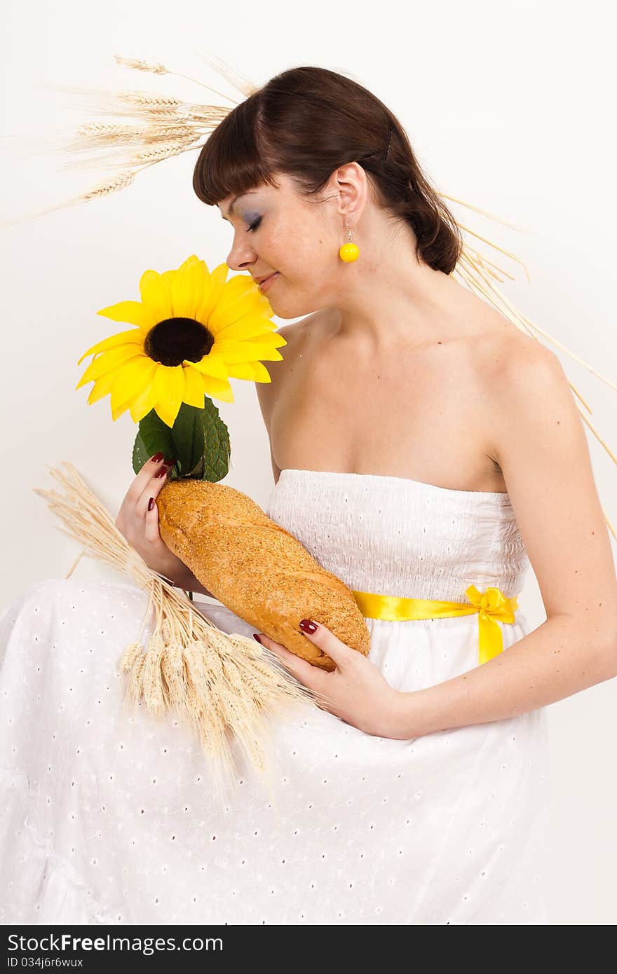 Beautiful brunette girl with sunflower and ears of wheat in her hair is eating a bread isolated on the white background. Beautiful brunette girl with sunflower and ears of wheat in her hair is eating a bread isolated on the white background