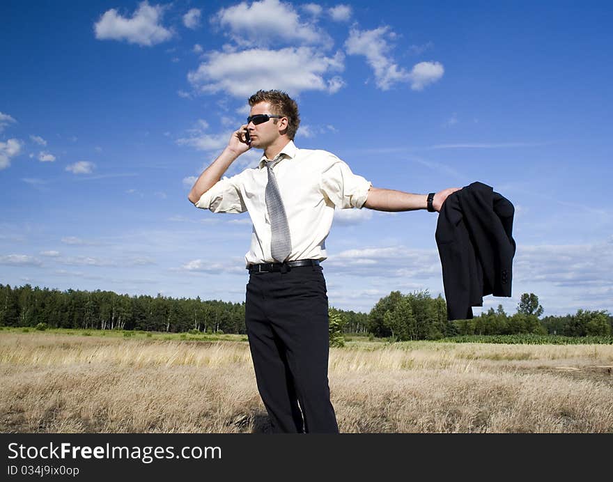 A businessman dressed in a smart suit standing on grass. Businessman talking on mobile phone