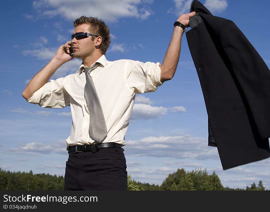 A businessman dressed in a smart suit standing on grass. Businessman talking on mobile phone