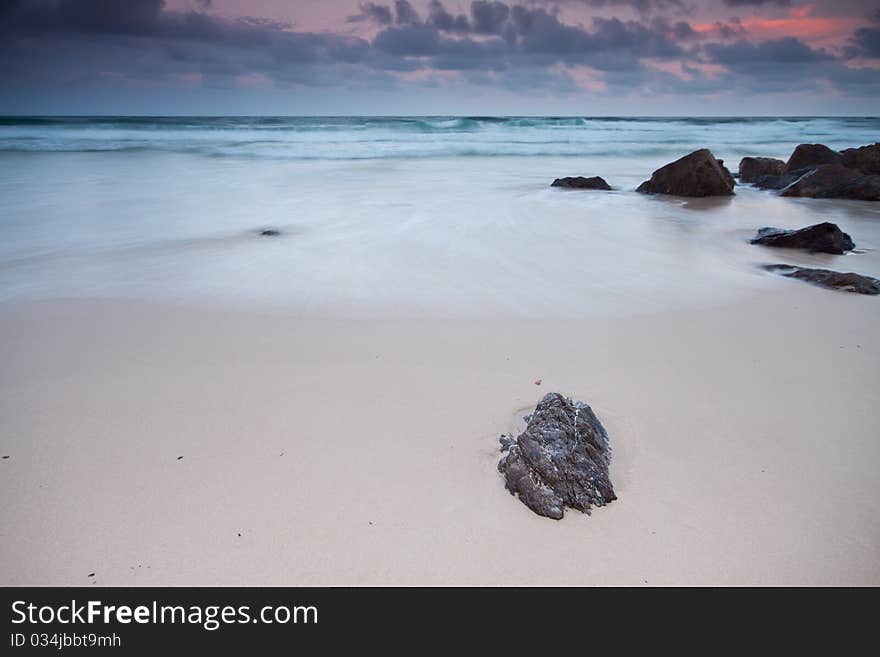 The beach at twilight with little rock in foreground