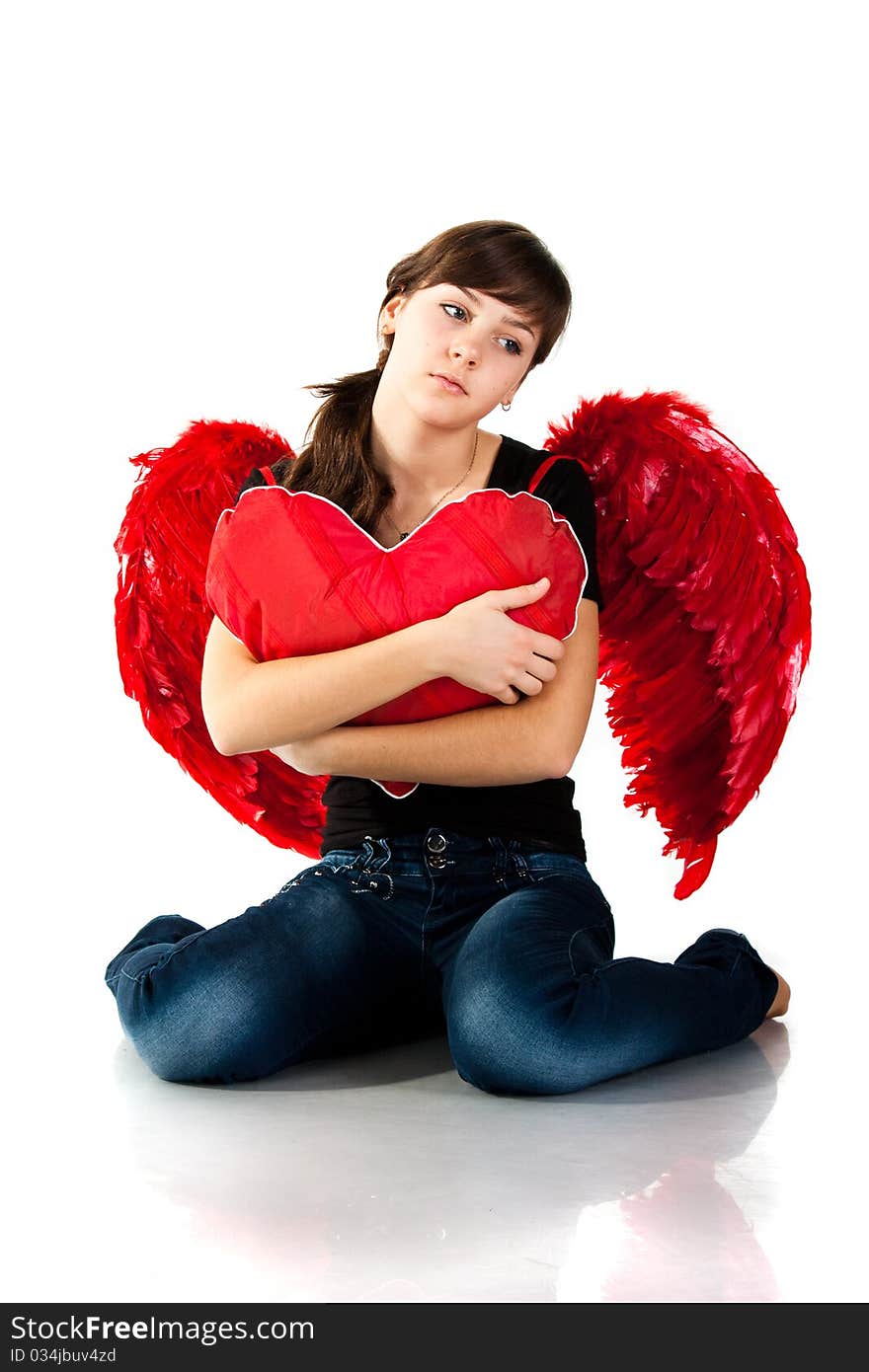 Beautiful girl sitting with heart shaped red pillow in red angel wings isolated on white