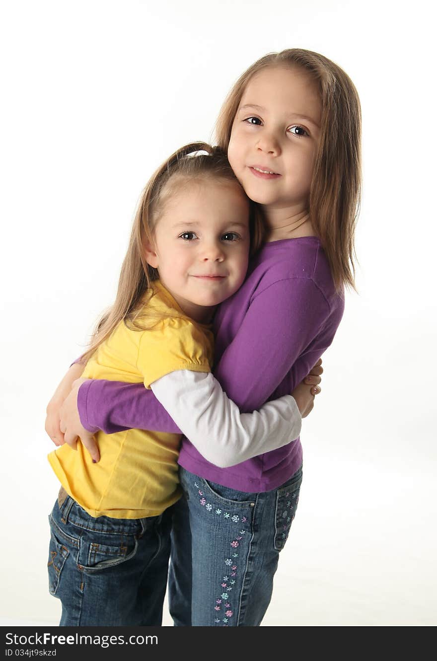 Two cute young sisters standing up hugging each other, isolated on white. Two cute young sisters standing up hugging each other, isolated on white