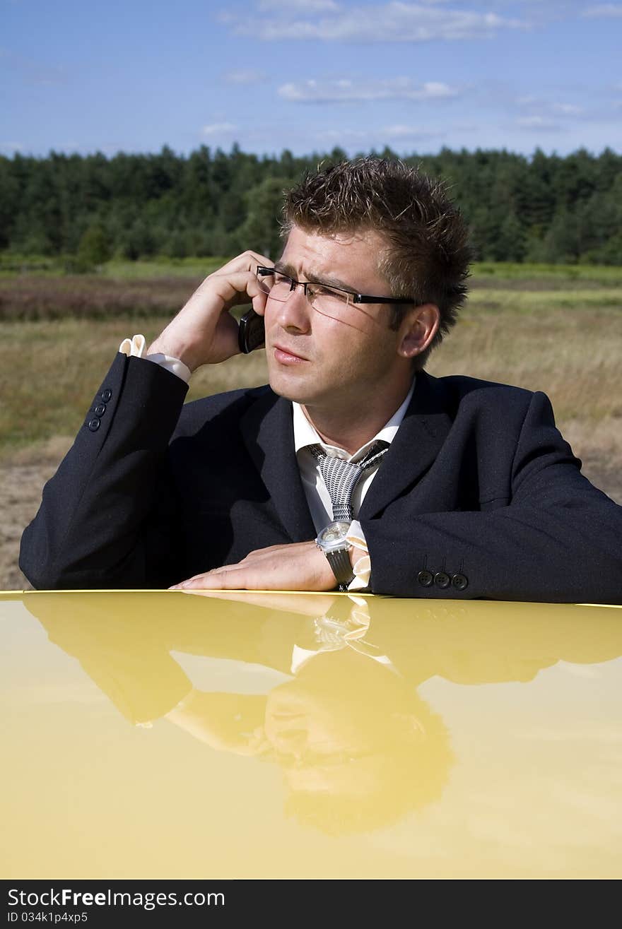 A businessman dressed in a smart suit standing on grass. Businessman talking on mobile phone