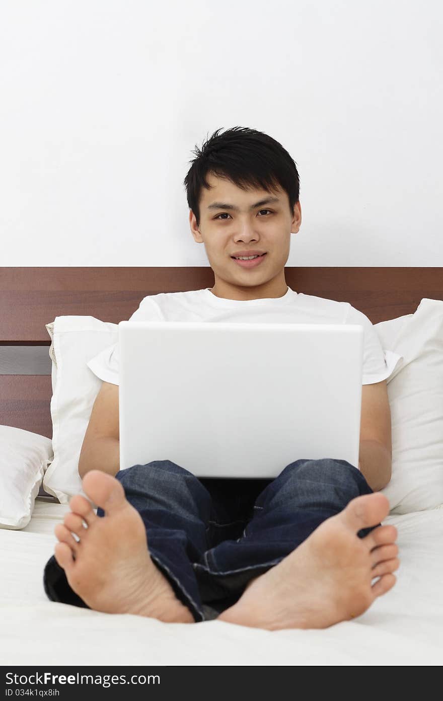 Young Asian man with laptop on a bed