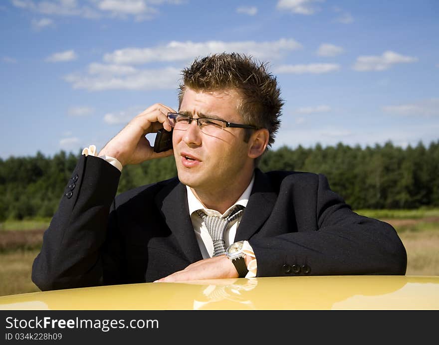 A businessman dressed in a smart suit standing on grass. Businessman talking on mobile phone