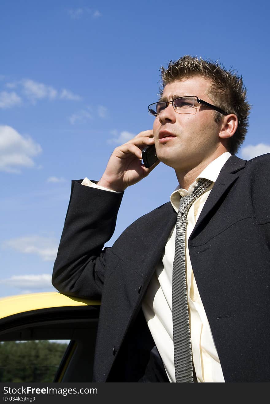 A businessman dressed in a smart suit standing on grass. Businessman talking on mobile phone