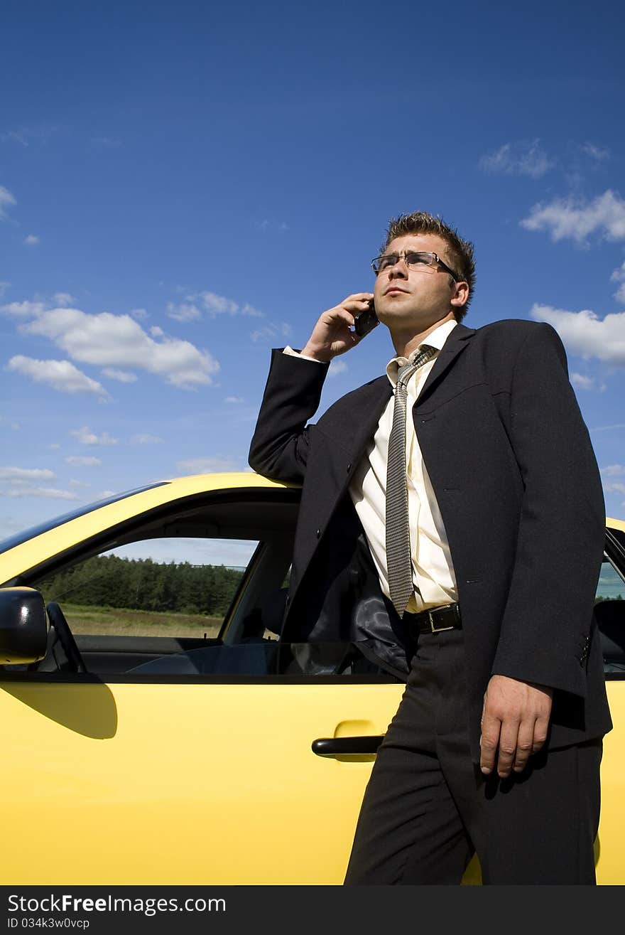 A businessman dressed in a smart suit standing on grass. Businessman talking on mobile phone