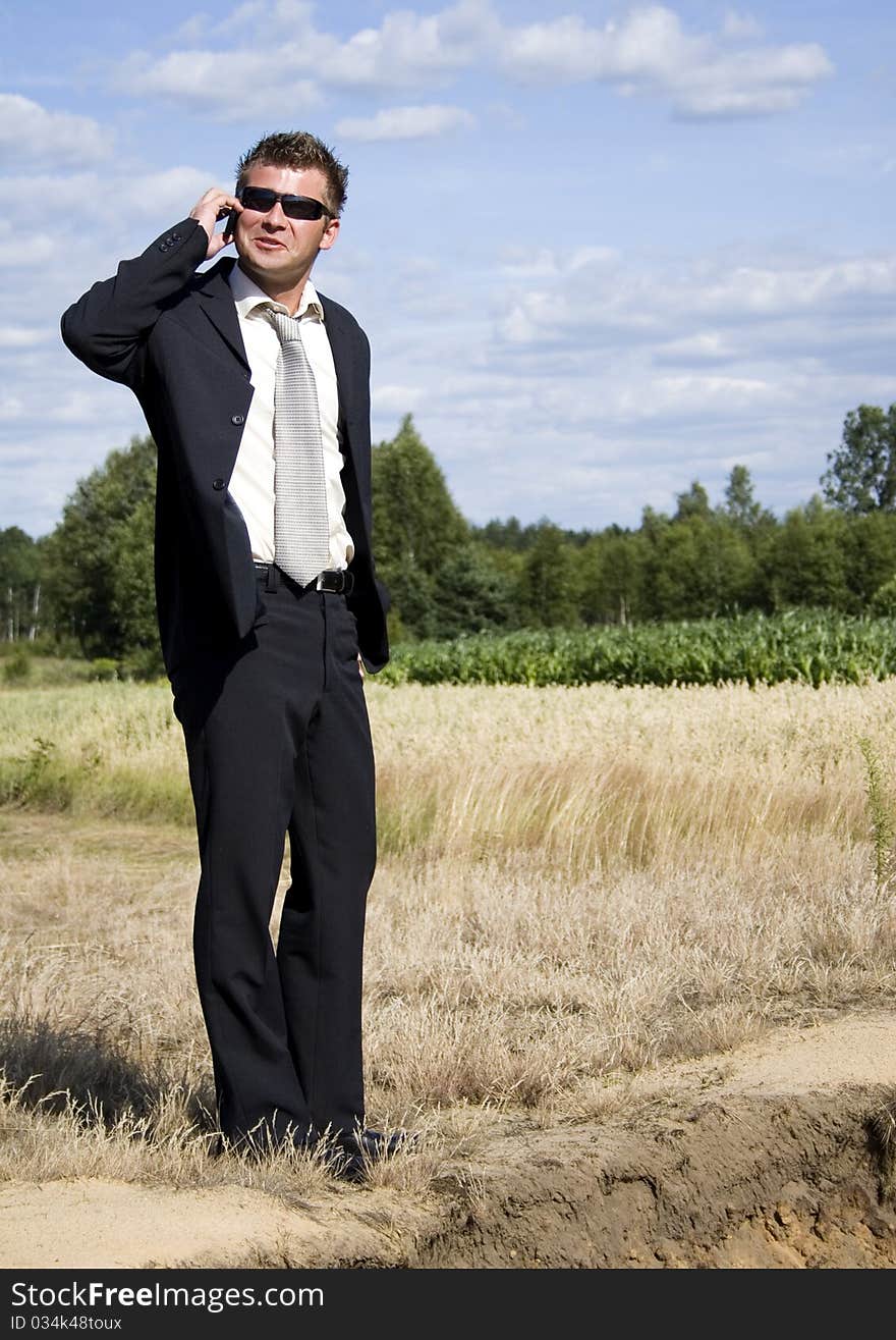 A businessman dressed in a smart suit standing on grass. Businessman talking on mobile phone