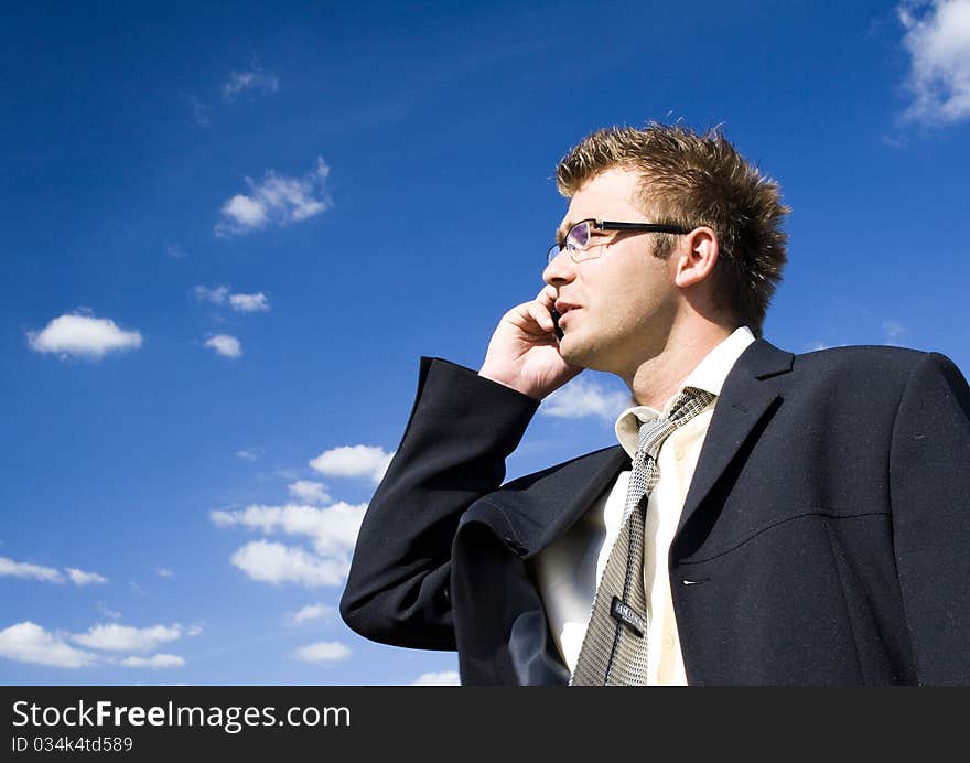 A businessman dressed in a smart suit standing on grass. Businessman talking on mobile phone