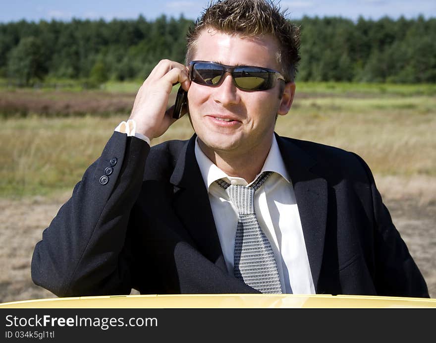 A businessman dressed in a smart suit standing on grass. Businessman talking on mobile phone