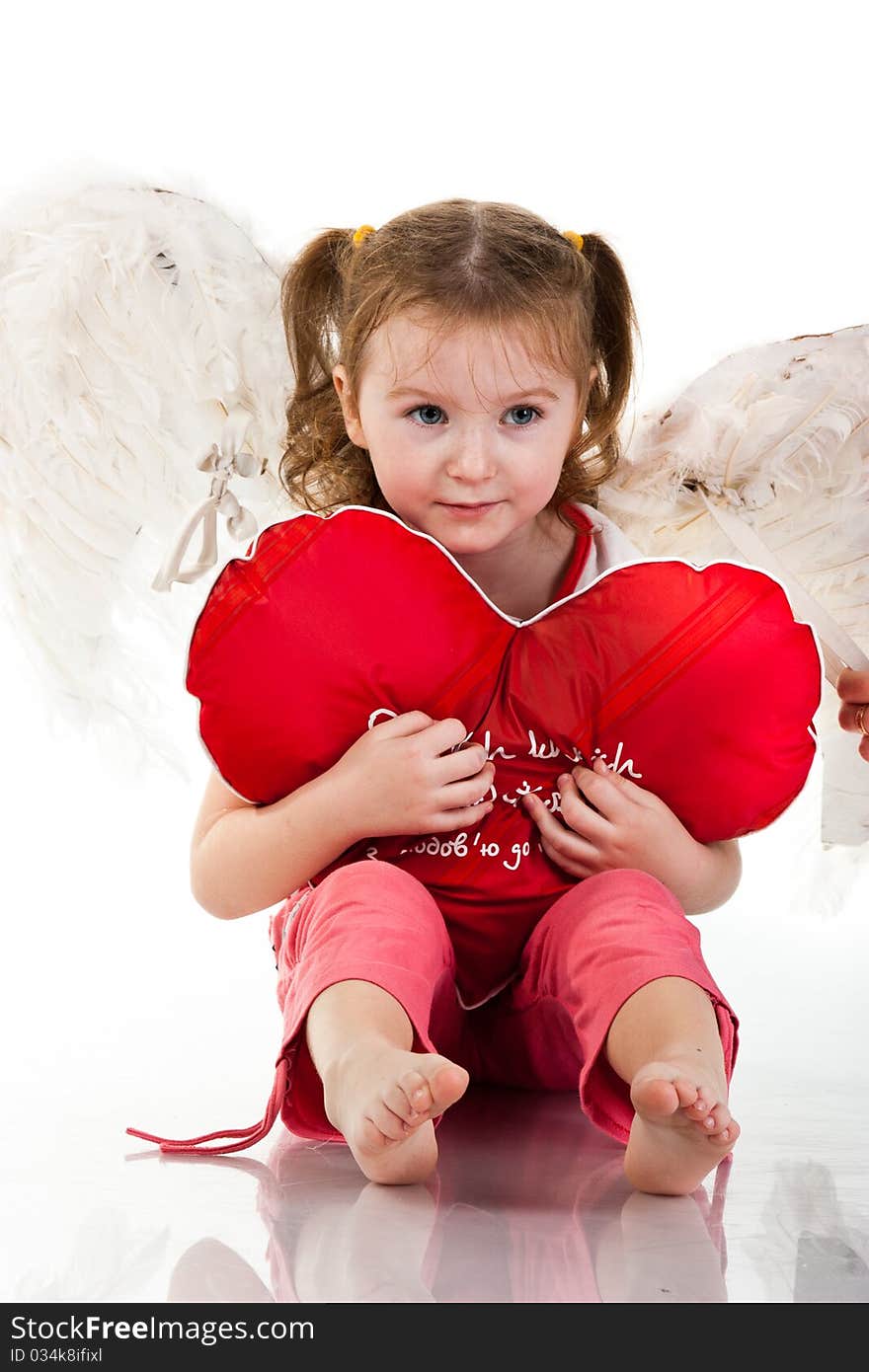 Beautiful girl sitting with heart shaped red pillow isolated on white