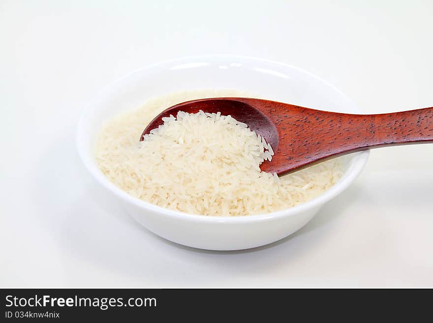 Rice grains in white bowl with brown wood spoon; white background.