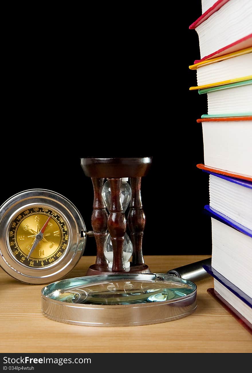 Pile of books, compass and hourglass on black background