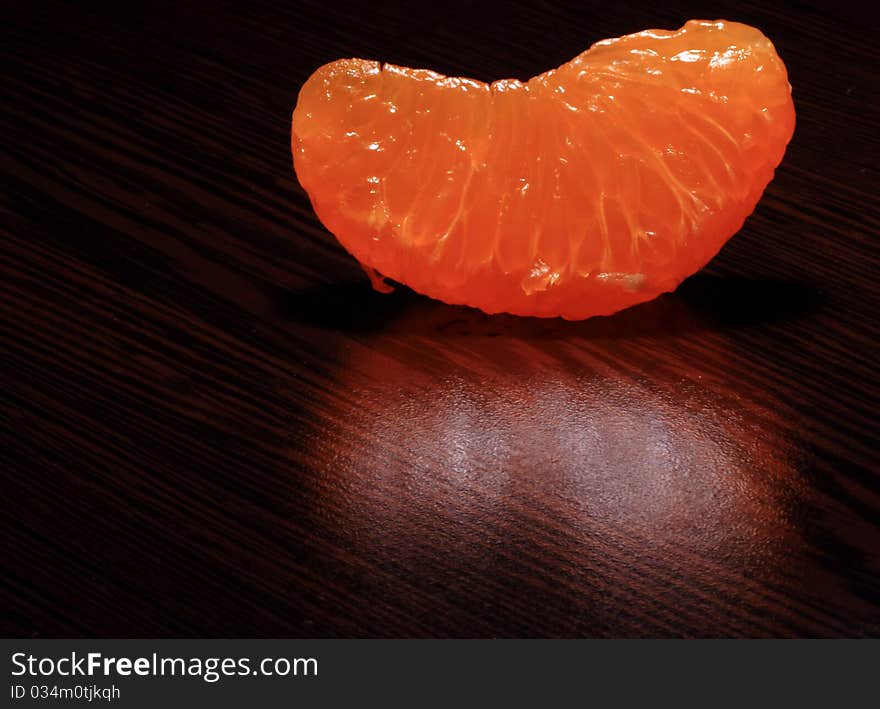 A peeled Tangerine segment on a dark brown wood table. A peeled Tangerine segment on a dark brown wood table