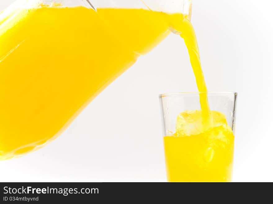 Orange cold drink poured from a glass container into a glass filled with ice. Orange cold drink poured from a glass container into a glass filled with ice