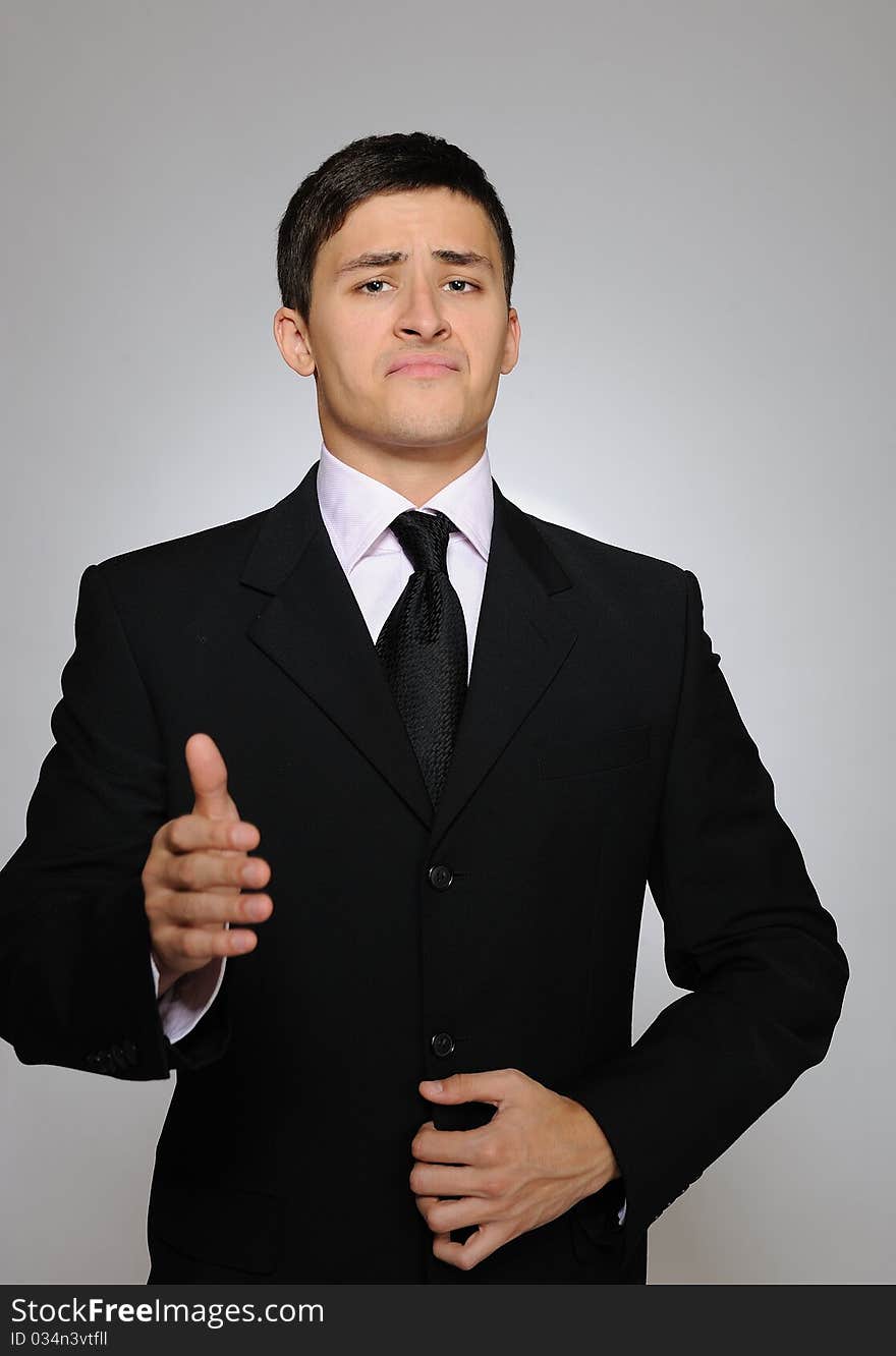 Young serious business man in black suit and tie. gray background