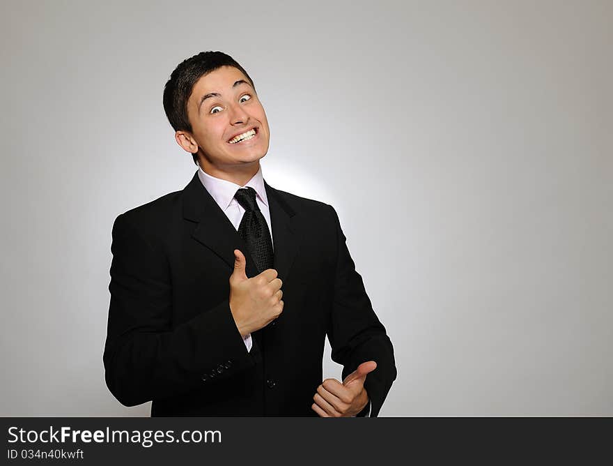 Young serious business man in black suit and tie. gray background