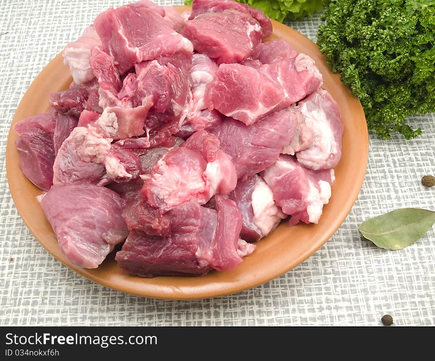 Meat cut by large pieces is in a plate on a kitchen table. Meat cut by large pieces is in a plate on a kitchen table