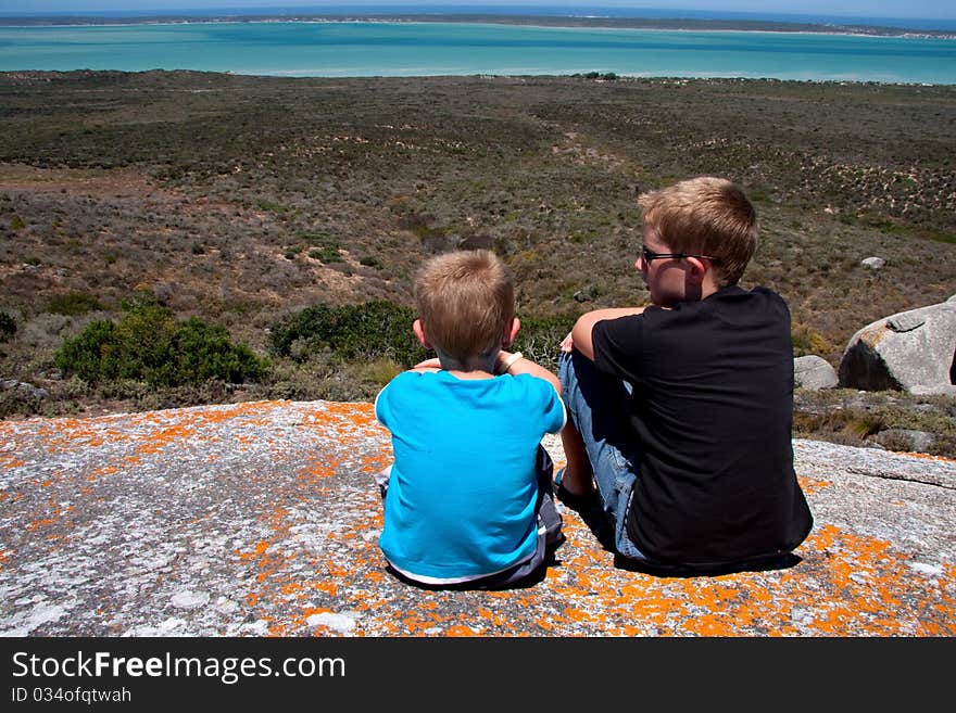 Brothers on vacation sitting on rock looking out over Langebaan lagoon in the westcoast national park in south africa. Brothers on vacation sitting on rock looking out over Langebaan lagoon in the westcoast national park in south africa