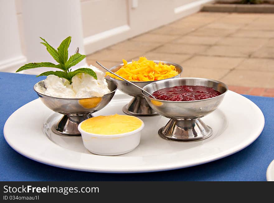 Condiments of cheese, cream, strawberry jam served with sconce in silver bowls on white plate in restaurant. Condiments of cheese, cream, strawberry jam served with sconce in silver bowls on white plate in restaurant