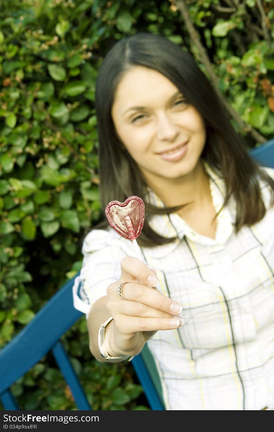 Young woman in an outdoors holding a lollipop in the shape of the heart. Sad. Young woman in an outdoors holding a lollipop in the shape of the heart. Sad