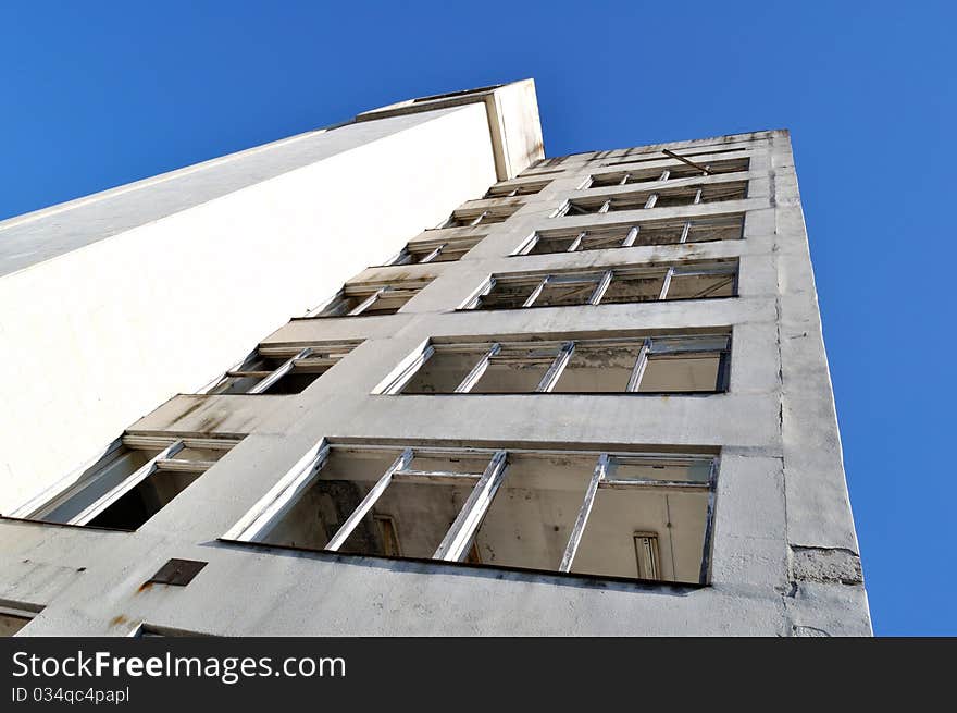 Damaged old grunge industrial building with broken windows upon blue sky