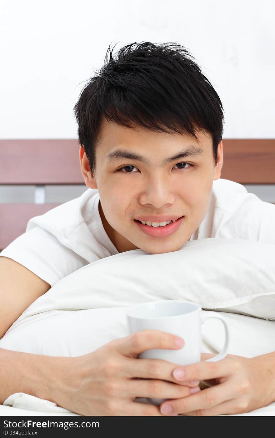 An Asian man having some coffee in bed. An Asian man having some coffee in bed