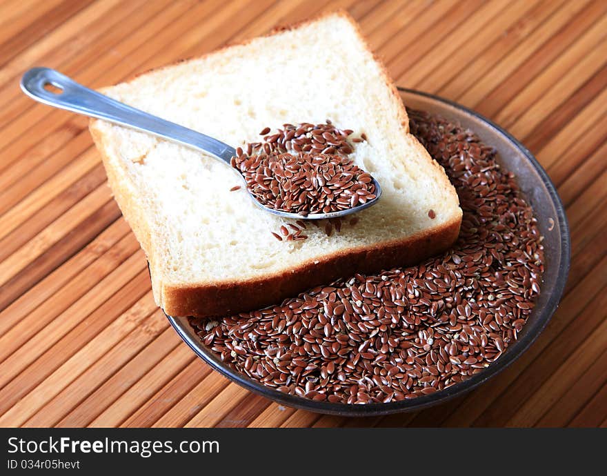 Closeup shot of bowl of raw linseed's with brown bread slice over wooden background. Closeup shot of bowl of raw linseed's with brown bread slice over wooden background.