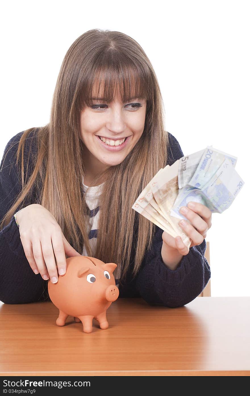 A young woman holding euro notes with a pig bank on the table. A young woman holding euro notes with a pig bank on the table