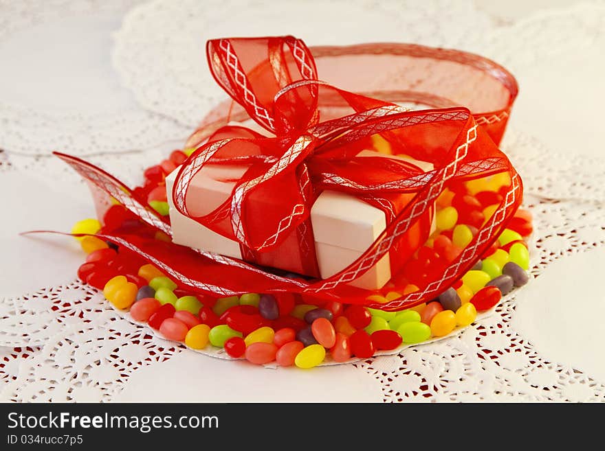 White package wrapped in red ribbon placed on colorful jellybeans and paper doilies. White package wrapped in red ribbon placed on colorful jellybeans and paper doilies