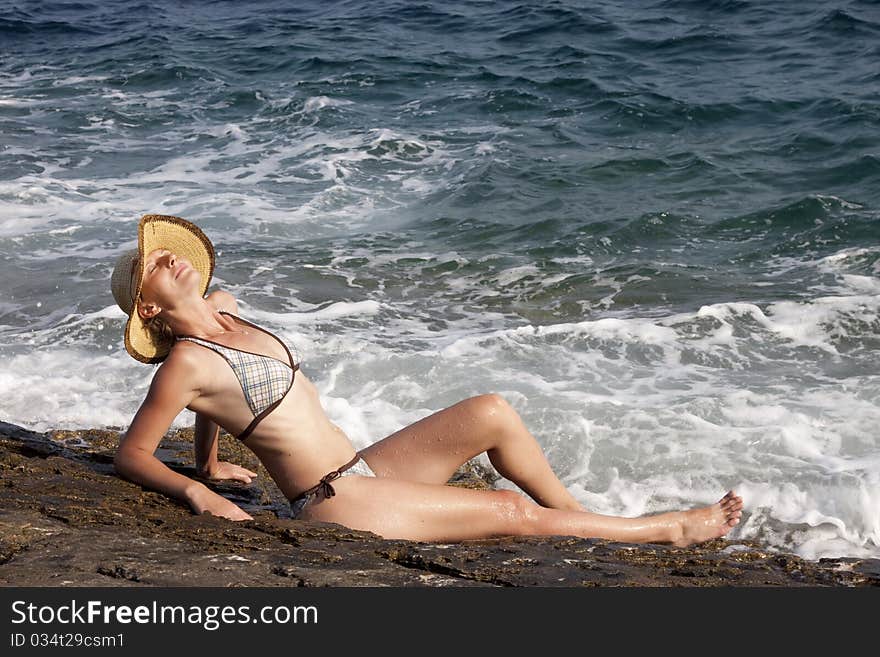 Woman with hat sitting on rocks near big waves