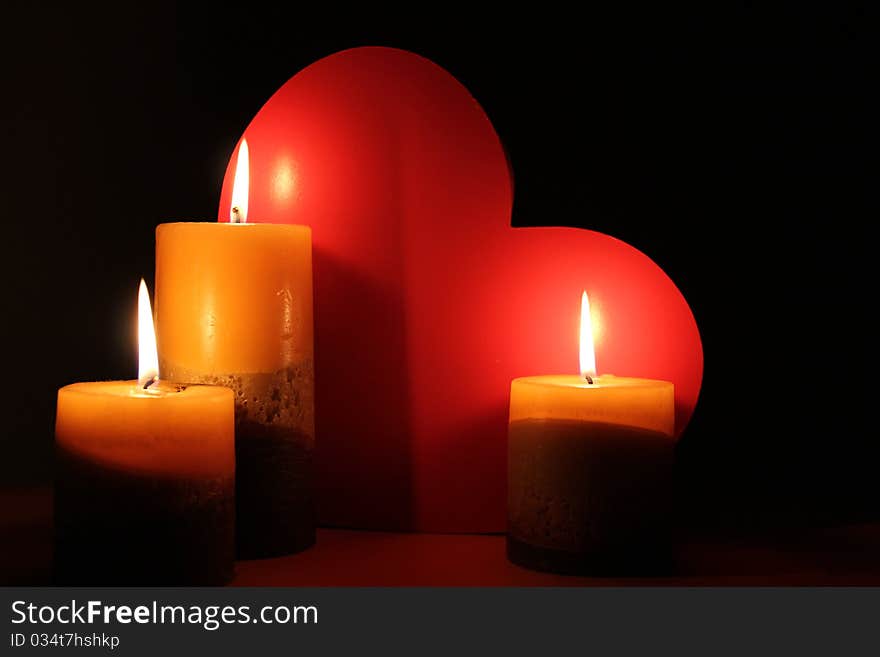 Lit Candles are illuminating a red love heart on a black background. Lit Candles are illuminating a red love heart on a black background