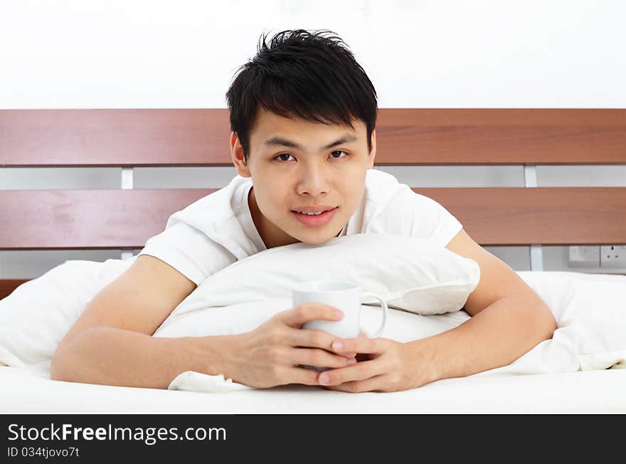 An Asian man drinking coffee in bed. An Asian man drinking coffee in bed