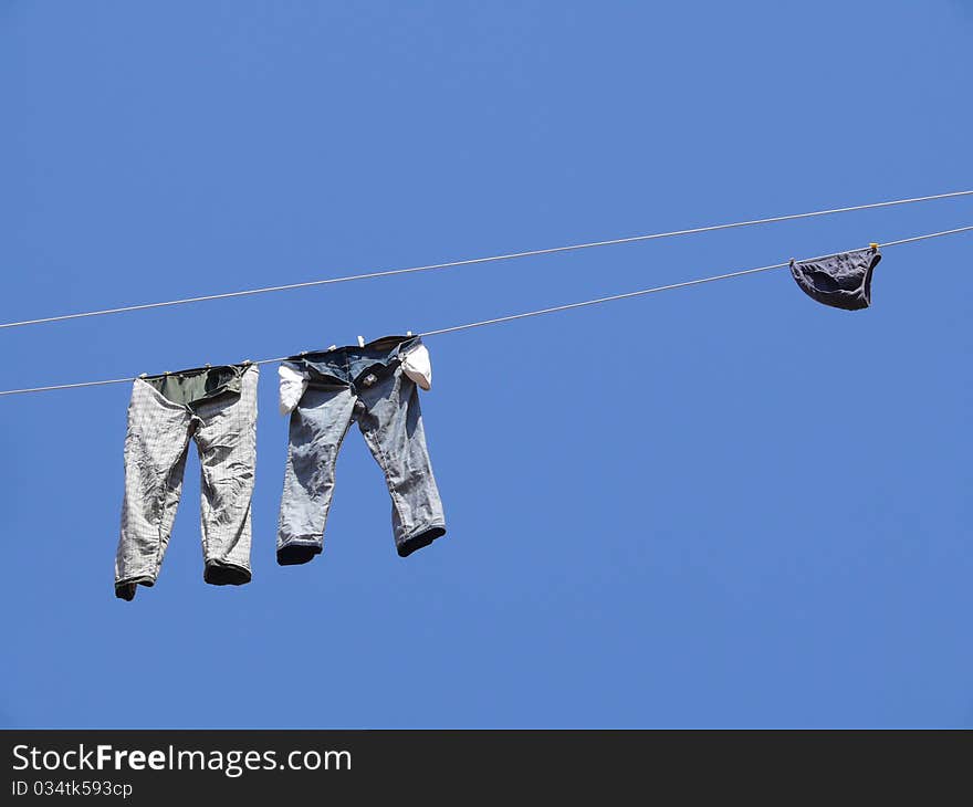 Jeans, trousers and men's swimming trunks are dried on the line against the blue sky. Jeans, trousers and men's swimming trunks are dried on the line against the blue sky