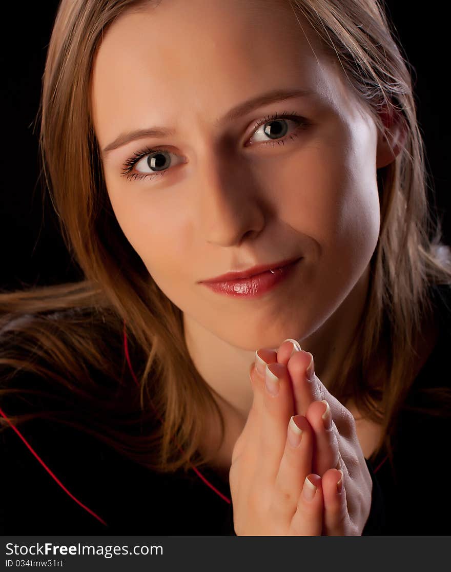 Beautiful young woman with hands folded asking for help on black background