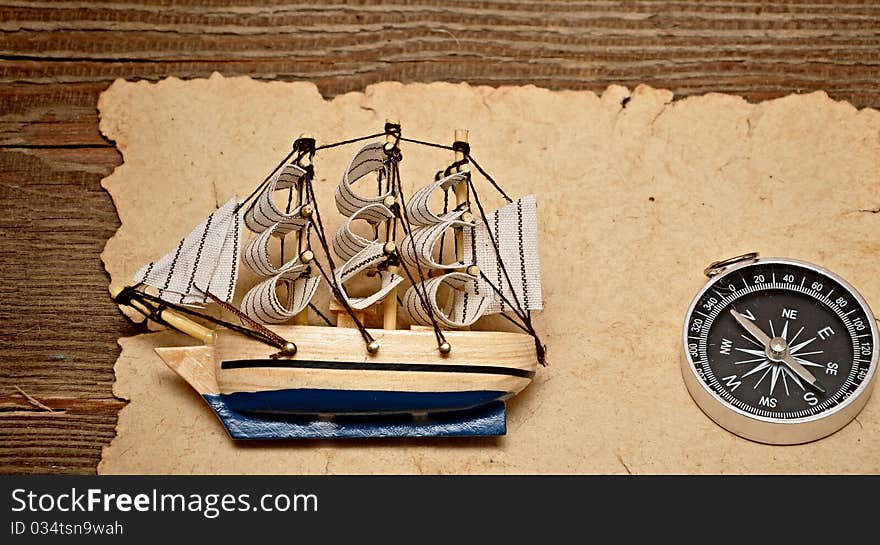 Old paper, compass, and model classic boat on wood background