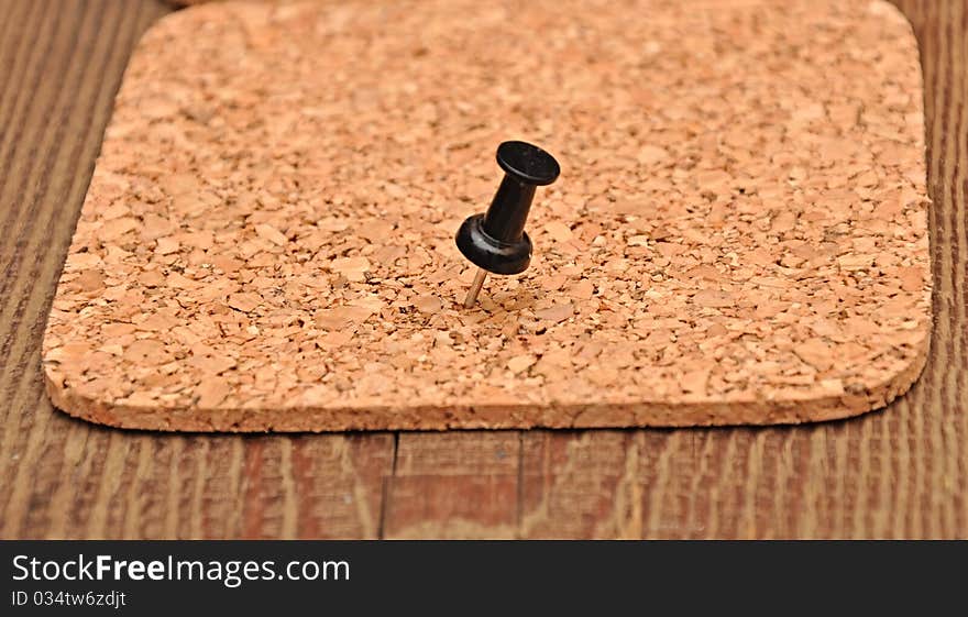 Cork texture pressed black pushpin on wood background